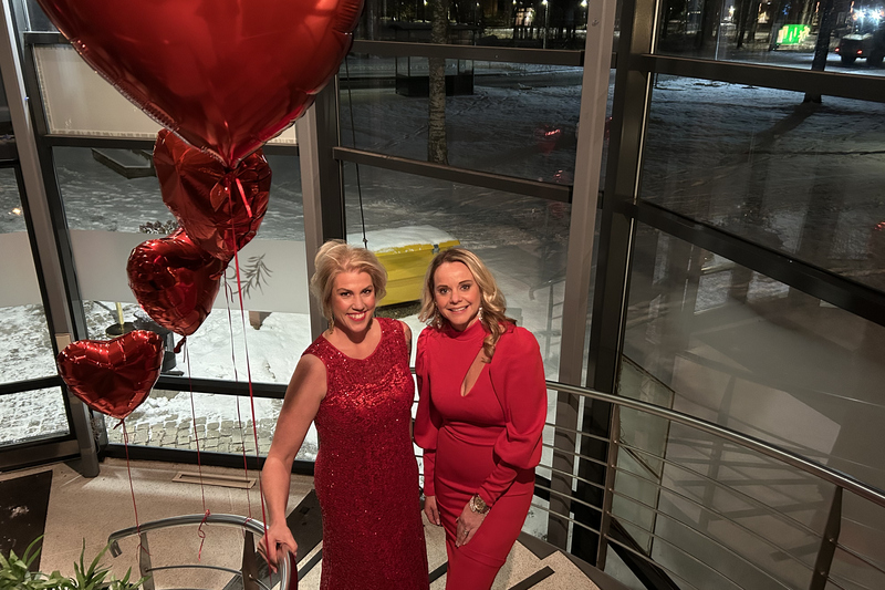 Två blonda kvinnor i röda klänningar står i en trapp