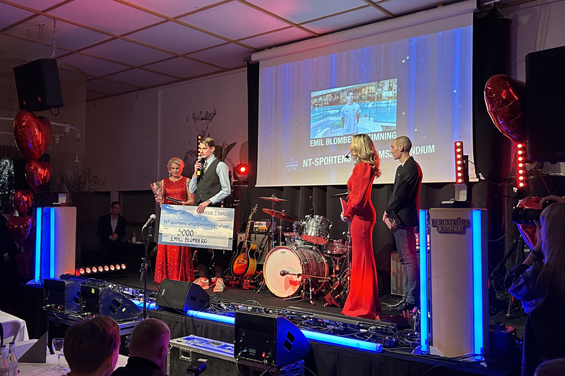 Fyra personer står på scen, en ung kille har en presentcheck i handen och pratar i mikrofon