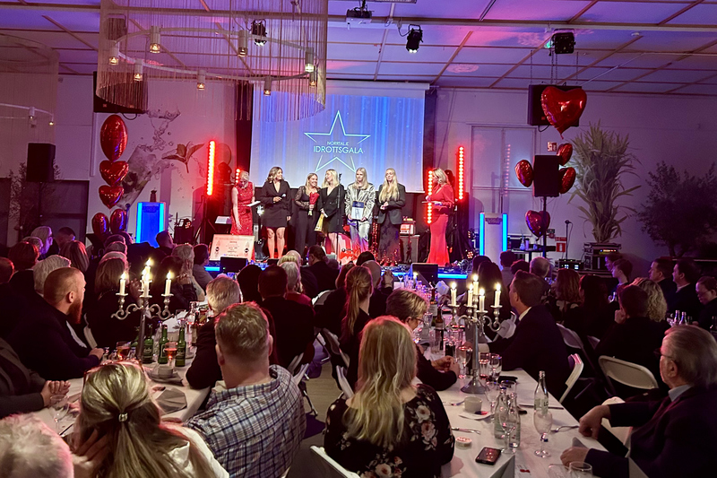 Publik som sitter vid ett bord och sex stycken kvinnor står på scen