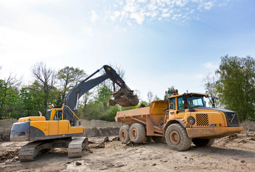 Grävskopa lastar jord på vagn.