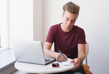Person med laptop, smartphone och anteckningsblock