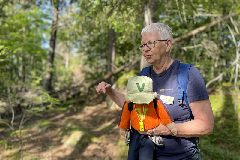 En kvinna st&aring;r med dockan vilse i skogen p&aring; F&auml;rsna naturreservat och h&aring;ller en guidning under invigningen av F&auml;rsna naturreservat och friluftslivets dag 27 augusti 2023