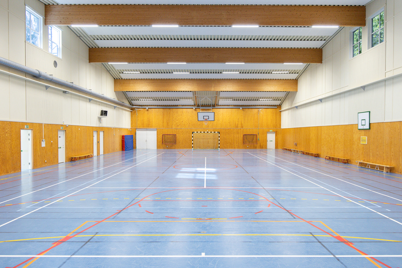 Stor sporthall med bl&aring;tt golv och basketkorg