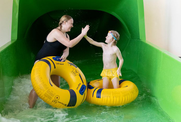 Två personer gör highfive i slutet av ruschkanan. De har gula badringar med sig som de åkt på.