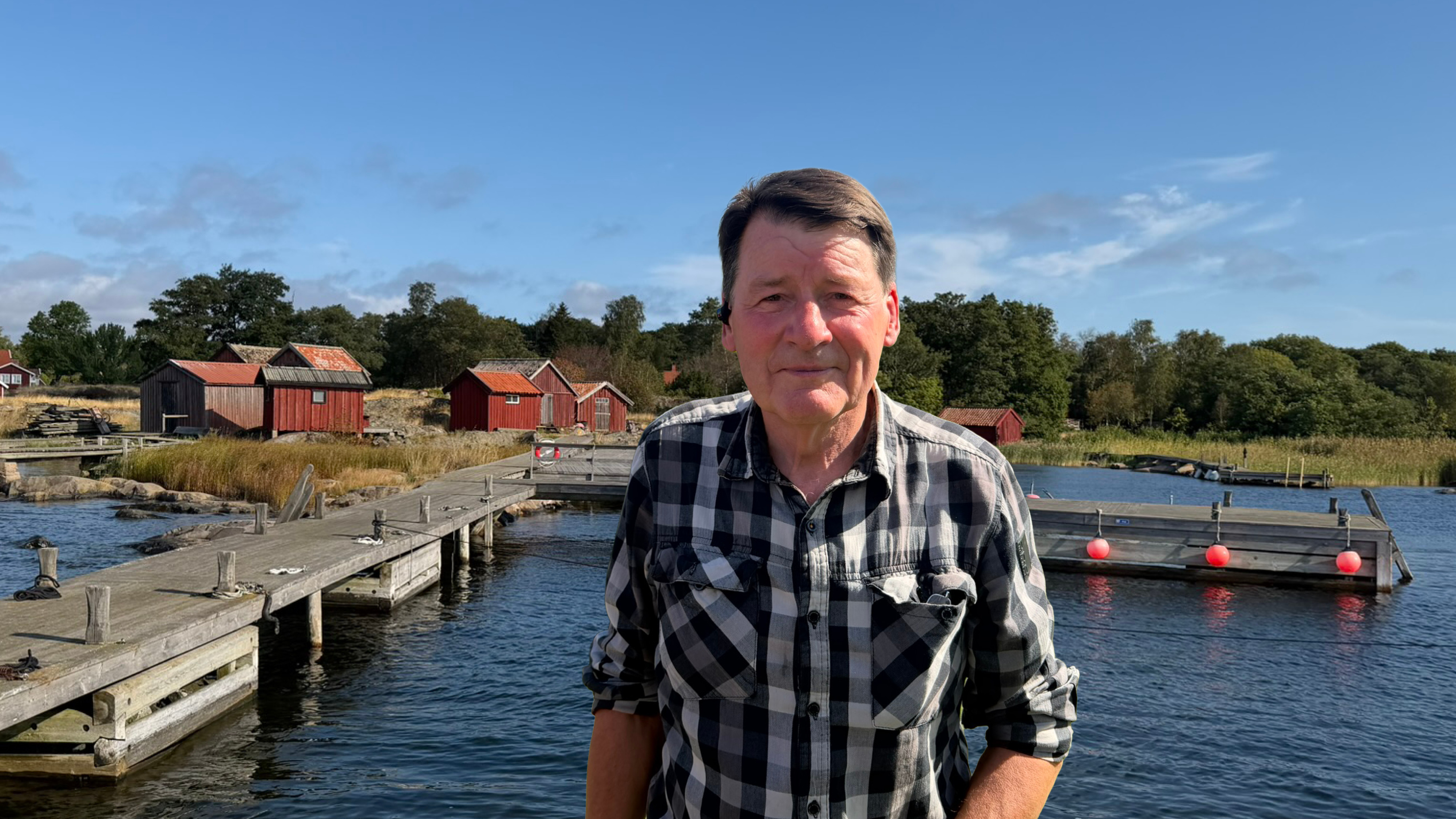 person st&aring;ende p&aring; brygga, i bakgrunden pittoreska r&ouml;da sj&ouml;stugor.