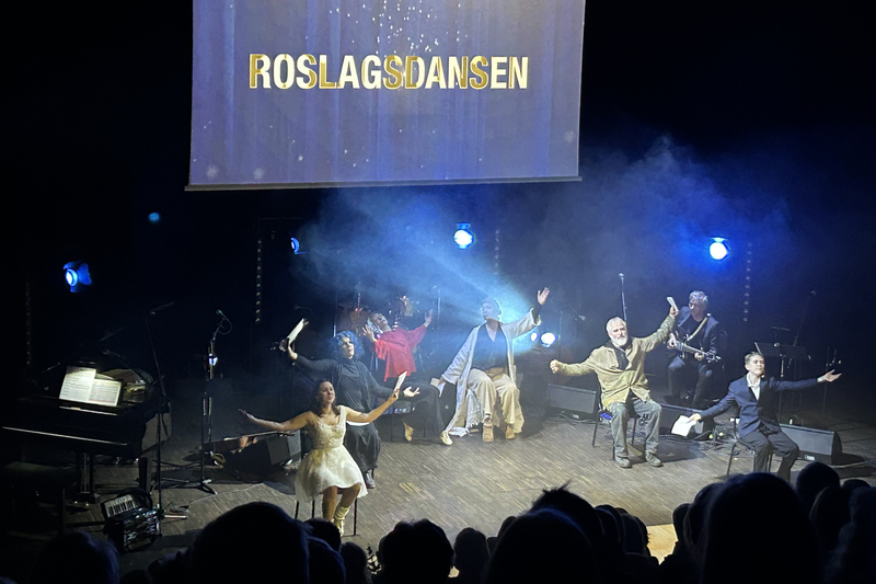 Upptr&auml;dande p&aring; scen. Sex personer sitter p&aring; stolar och str&auml;cker ut sina armar