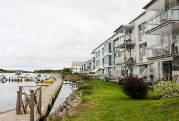 Gråvitt flerfamiljshus med träfasad och inglasade balkonger utmed vattnet