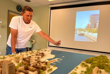 Man står vid en trämodell av Norrtälje hamn medan ett bildspel med bilder från hamnen visas på väggen bakom