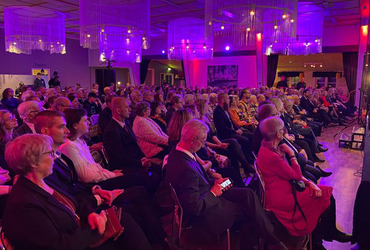 Sittande publik i en stor neonupplyst festlokal