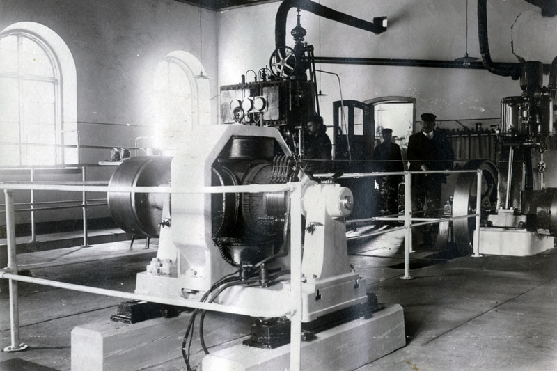 Historisk svartvit bild. Tv&aring; herrar st&aring;r inne i industribyggnaden.