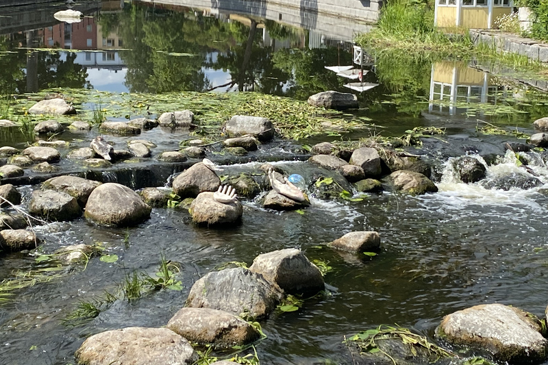 En rinnande &aring; med massor av stenar. I mitten ligger tv&aring; skulpturer som &auml;r tv&aring; h&auml;nder och den ena handen h&aring;ller i en genomskinlig p&auml;rla.
