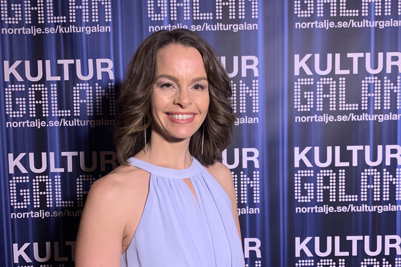 Hilda Henze i bl&aring; kl&auml;nning st&aring;r framf&ouml;r en bl&aring; bakgrund d&auml;r det st&aring;r kulturgalan p&aring;.