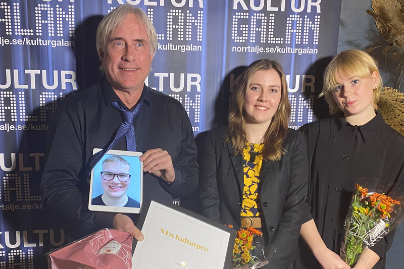 Tre personer står framför totoväggen som är blå. Bengt Hilding håller i en ipad som visar en pojkes ansikte. Bredvid honom står två unga tjejer.