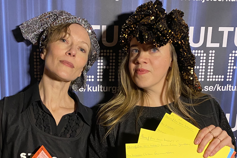 Bilden visar två tjejer som håller i manuskort. Tjejerna har glittriga turbaner på huvudet.