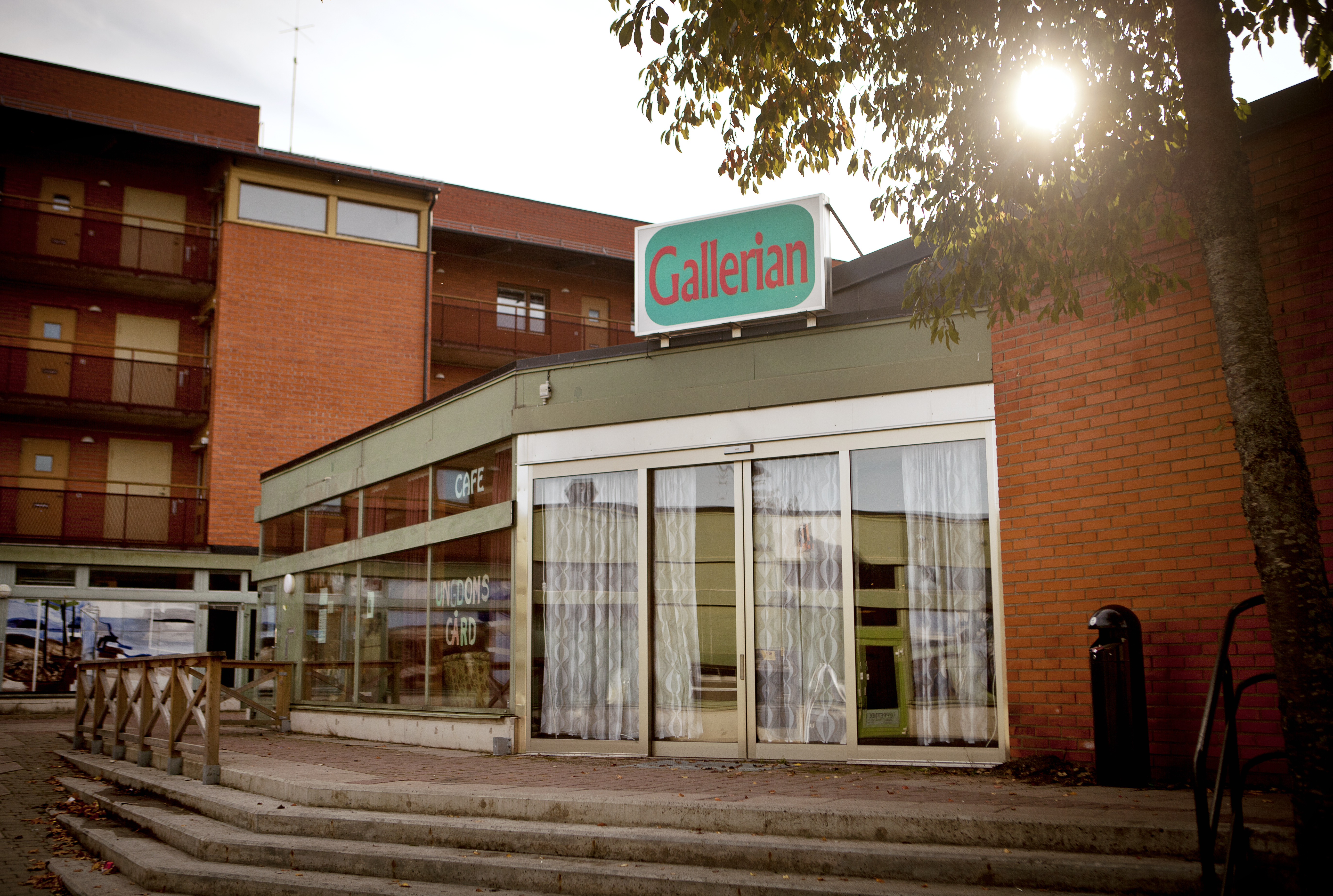Tegelbyggnad med stora glasfönster. På taket sitter en turkos skylt där det står Gallerian