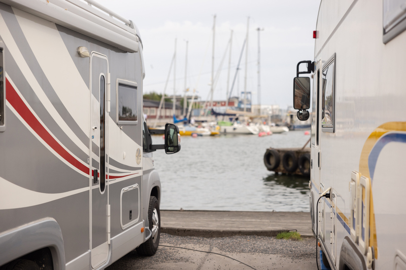 tv&aring; husbilar st&aring;r parkerade med fronten mot en kaj. I bakgrunden syns b&aring;tar och en brygga.