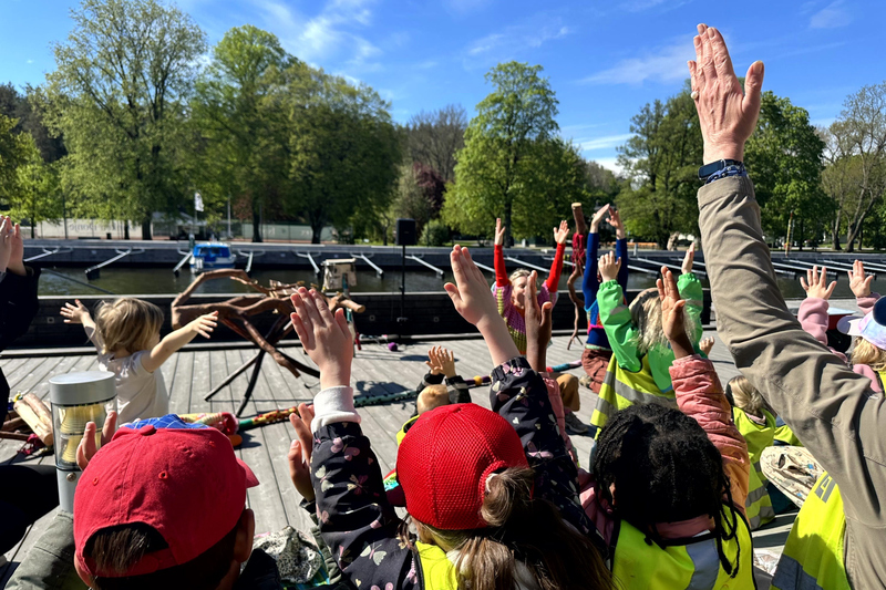 Barn och pedagoger deltar i dansen med uppstr&auml;ckta h&auml;nder i luften