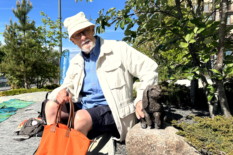 En man med hatt och en orange v&auml;ska klappar en kanin i brons