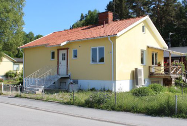 Gult fyrkantigt hus med liten trädgård