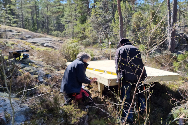Tv&aring; personer hj&auml;lps &aring;t att bygga en tr&auml;plattform mitt ute i skogen.