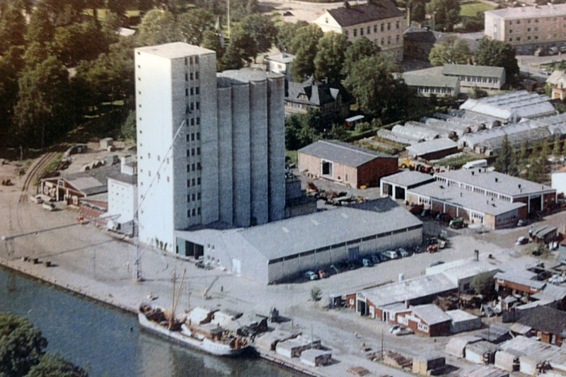 Flygbild &ouml;ver hamnen och silo. Bilden &auml;r tagen omkring 1965 och p&aring; bilden syns hamnkajen med lastfartyg. Industribyggnader ses runt om silon och l&auml;ngre bak i bilden syns bostadshus.